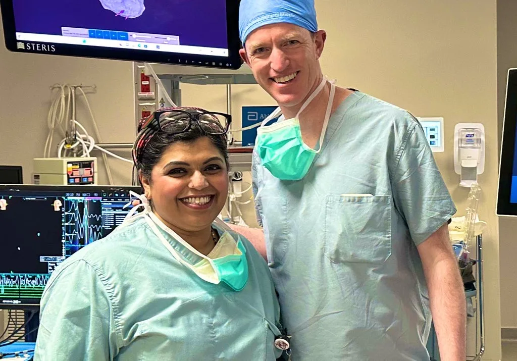 Two clinicians in scrubs standing in a cardiac catheter lab