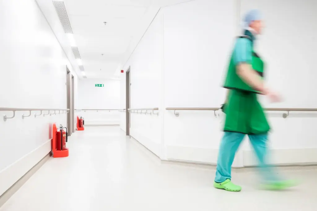 Hospital staff member in scrubs walking along a ward corridor